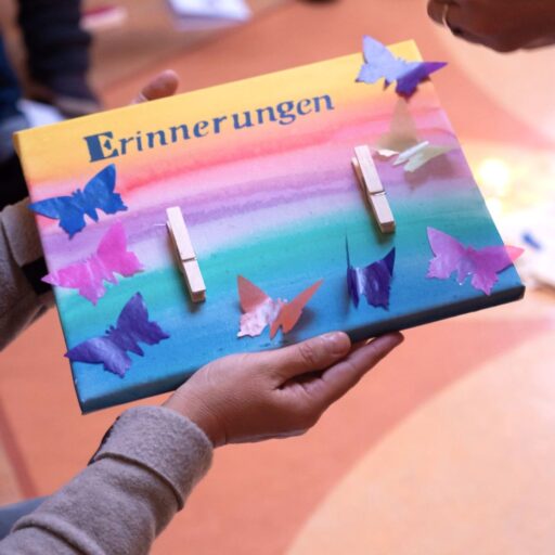 Ein Bild mit einem gemalten Sonnenuntergang, dem Wort Erinnerung und aufgeklebten Schmetterlingen aus Papier